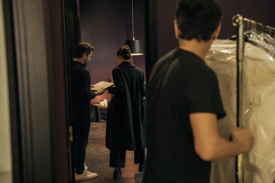 End of a night shoot: a producer hands a model her copy of the signed booking paperwork at the studio door while an assistant wheels a garment rack past