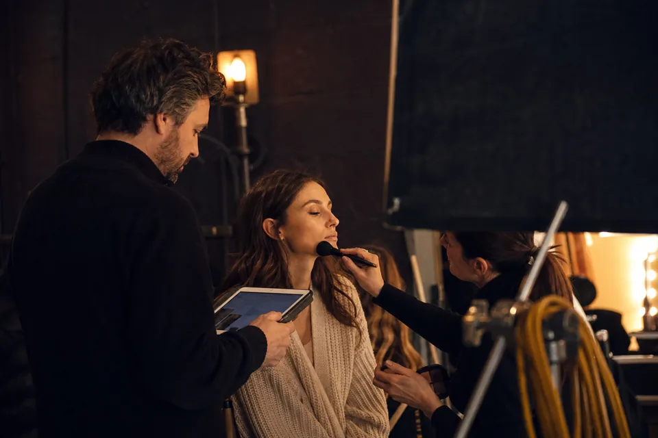 On set: a producer checks the call sheet on a tablet while a model gets a final touch-up before the first frame